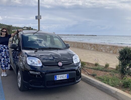 Auto nera Fiat Panda di Stallone Rent SRL parcheggiata sul lungomare con una donna appoggiata, ideale per esplorare la costa italiana.