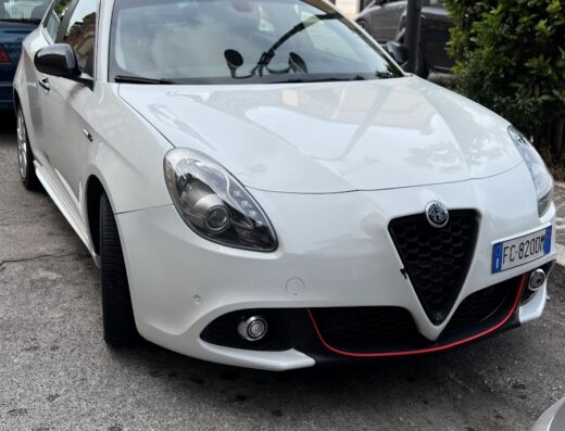 Stazione di Servizio ed Autolavaggio Self H24 Corsi Carburanti SRL: Alfa Romeo Giulietta bianca parcheggiata in strada, con cartello pubblicitario sullo sfondo, ideale per servizi auto e marketplace.