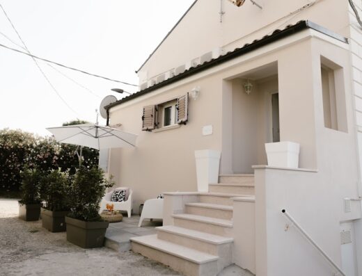 Esterno di una casa vacanze con ombrellone, sedie da esterno e piante in vaso, ideale per relax e soggiorno in stile STAZIONEAMARE.