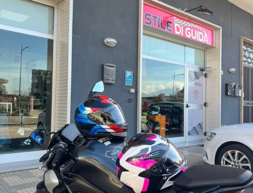 Moto nera parcheggiata di fronte al negozio Stile Di Guida con due caschi da moto colorati, accessori per motociclisti e vendita di ricambi