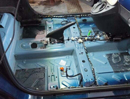 Interno di un'auto in fase di riparazione o personalizzazione, con la moquette rimossa per interventi di style auto o manutenzione approfondita.