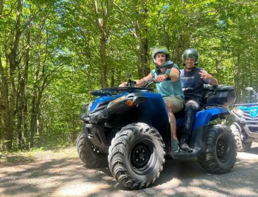 Due persone con casco su un quad blu in un contesto boschivo. Esperienza di viaggio e avventura con SudXtreme.