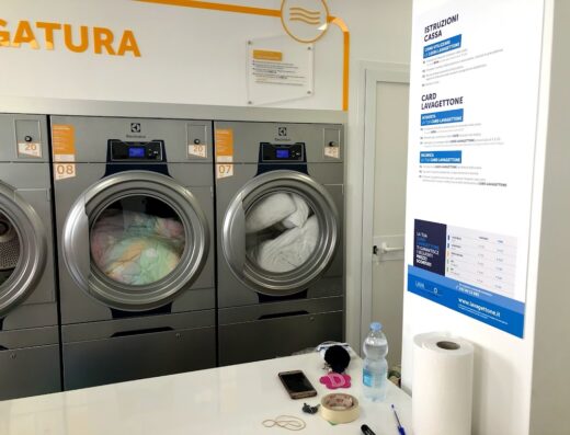 Interno di Sun Wash s.r.l. con lavatrici Electrolux in funzione, istruzioni cassa e card Lavagettone, accessori e prodotti per il lavaggio a gettone.