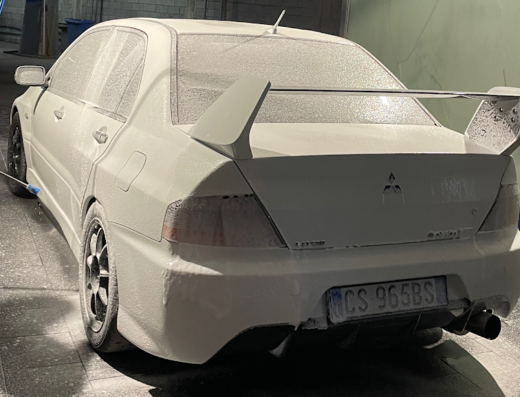 Lavaggio auto professionale presso Sun Wash Srl: una Mitsubishi Lancer Evolution bianca viene pulita con idropulitrice e schiuma, dettaglio dello spoiler e della targa italiana 'CS 965BS'