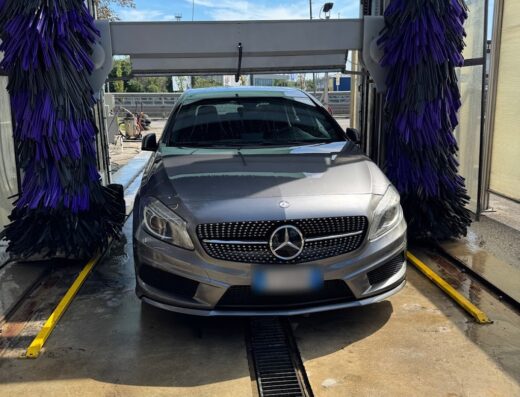 Auto grigia in un autolavaggio automatico con spazzole rotanti viola e nere, per una pulizia professionale del veicolo.