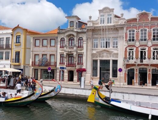 Gondole colorate attraccate lungo il canale a Aveiro, Portogallo, con edifici storici sullo sfondo, offrendo tour turistici unici.