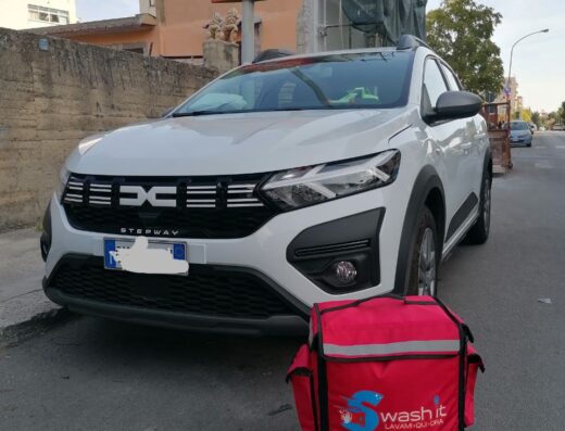 Auto bianca Stepway con borsa termica rossa Swash it per autolavaggio a domicilio parcheggiata su strada cittadina.