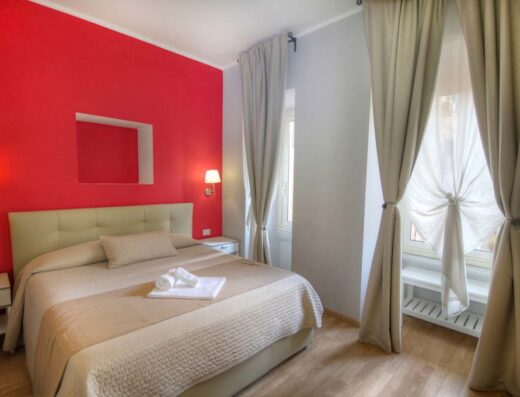 Camera da letto accogliente a Sweet Home Faleria, con pareti rosse vivaci, letto matrimoniale confortevole, tende eleganti e illuminazione calda.