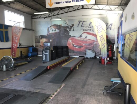 Interno del Te.Sa.Via Centro Revisioni con ponte sollevatore per moto, attrezzatura controllo freni e insegne pubblicitarie.