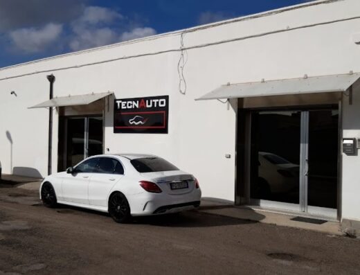 Tecnauto: officina specializzata in servizi auto e moto. In primo piano, una Mercedes bianca e un furgone Fiat parcheggiati di fronte all'ingresso dell'officina.