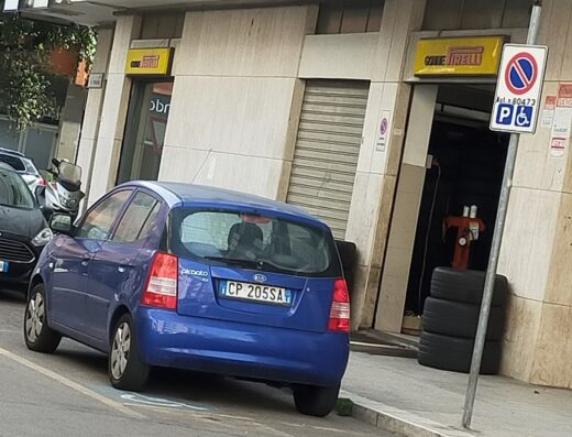 Tecnigom Via del Mare R17: Auto blu parcheggiata di fronte all'officina con insegna "Officine Pirelli", servizi di riparazione e vendita pneumatici.