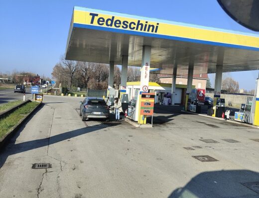 Stazione di servizio Tedeschini Carburanti con auto parcheggiata per il rifornimento, prezzi carburante in evidenza, cielo sereno.