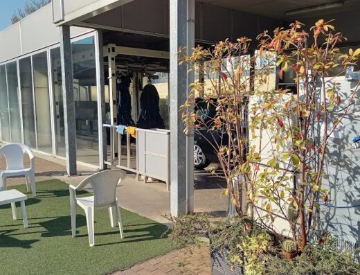 Teler: Area di servizio con autolavaggio self-service per moto e auto. Sedie e tavolino per i clienti in attesa.