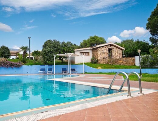 Piscina presso Tenuta Guparza con vista sulla casa in pietra e area relax con lettini, circondata da vegetazione e cielo azzurro.