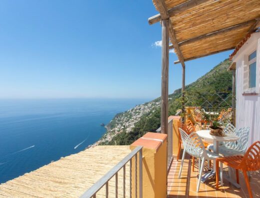 Vista mozzafiato dalla terrazza di Tenuta La Picola, con tavolo e sedie colorate affacciate sul mare e sulla costa di Positano.