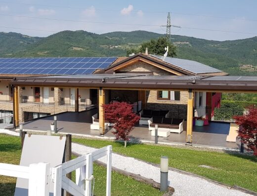 Tenuta Valdorso Agri-Resort exterior view featuring solar panels on the roof, outdoor patio furniture, landscaped grounds, and mountain backdrop.