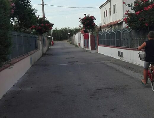 Strada residenziale a Termoli con un ragazzo in bicicletta, case con fiori e vegetazione, ideale per ricambi moto e accessori viaggio.