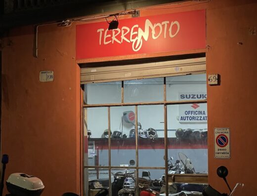Foto notturna dell'officina Terremoto Motocicli e Scooter, con vetrina che espone moto, scooter e caschi, e cartello Suzuki Officina Autorizzata.
