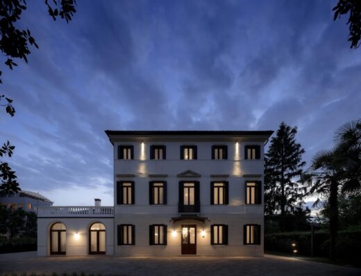 The Foscarini building, a three-story white building with dark shutters, illuminated at dusk against a cloudy sky.