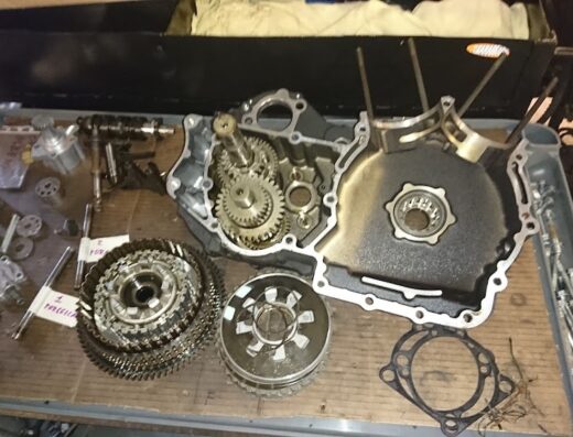 Ricambi e componenti del motore di una moto smontato sul banco da lavoro di The Garage snc, inclusi ingranaggi, frizione e bulloni, per riparazione o manutenzione