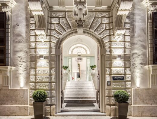 Ingresso elegante del Liberty Boutique Hotel, con architettura in pietra chiara, scalinata interna e illuminazione suggestiva. Dettaglio del numero civico e insegna dell'hotel.