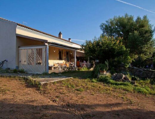 La Vecchia Fattoria Asfodeli, una casa di campagna in Sardegna con veranda arredata, giardino curato e cielo azzurro.