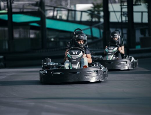 Due persone che guidano go-kart neri su una pista all'aperto. Caschi di protezione e illuminazione a LED sui kart visibili. Esperienza di karting emozionante e diversa.