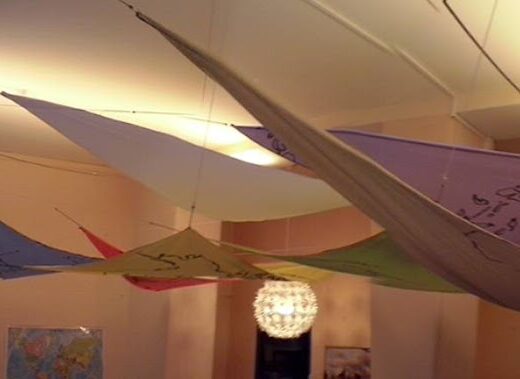 Installazione artistica con tessuti colorati sospesi al soffitto, illuminati da una lampada decorativa. Ti Emme Travel interior design.