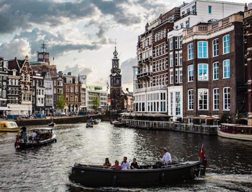 Amsterdam: Scorcio di canale con barche di turisti e architettura storica, offerto da Tiarè Viaggi, agenzia di viaggi e tour operator.