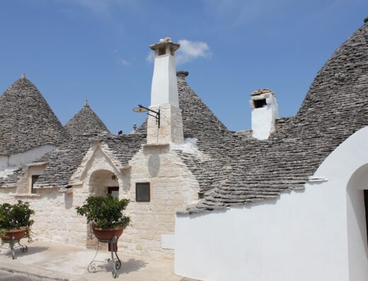 Tipico resort in trulli ad Alberobello, Puglia, Italia: caratteristici edifici con tetti conici in pietra grigia, dettagli architettonici unici e piante ornamentali.