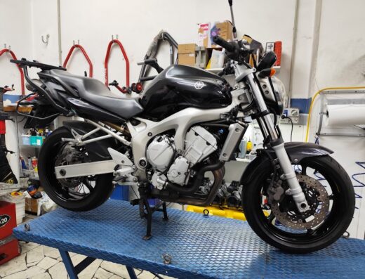 Yamaha FZ6 nera su un ponte sollevatore blu in officina, pronta per manutenzione o riparazione. Moto naked ideale per viaggi e uso urbano.