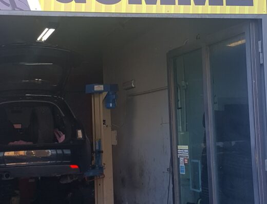 Tonino Gomme: vista dell'officina che offre servizi di riparazione e sostituzione pneumatici. Un'auto è sollevata su un ponte.