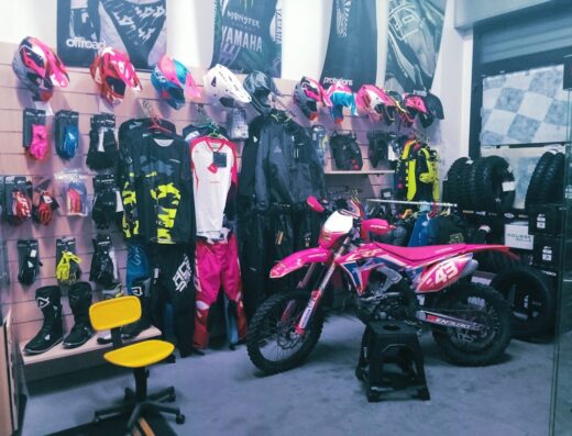 Negozio Tony Moto: moto da cross Honda CRF rosa personalizzata in esposizione, accessori e abbigliamento tecnico per motociclisti, caschi, stivali, pneumatici enduro