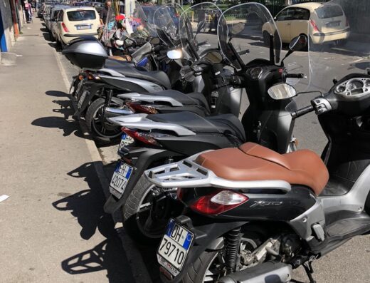 File di scooter parcheggiati lungo una strada in Italia, con targhe ben visibili, ideali per il noleggio moto e la mobilità urbana.