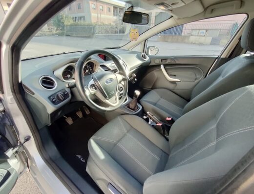 Interni di una Ford Fiesta, con volante, sedili e cruscotto visibili. Accessori auto e dettagli interni ben puliti.