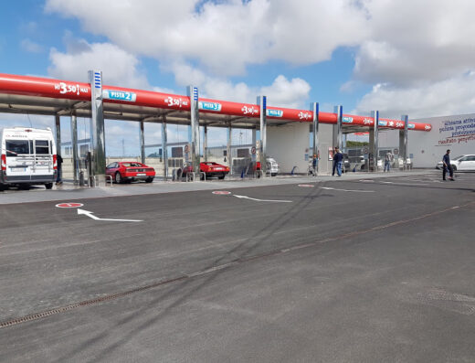 Top Wash Pisa car wash facility with multiple washing bays, including a van, two red Ferrari sports cars, other cars and people using the self-service car and motorcycle wash.