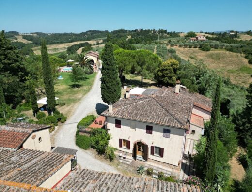 Vista aerea di Torre Rasa, una casa colonica toscana con piscina, situata in un paesaggio collinare con alberi di cipresso e uliveti.