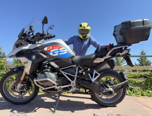 Un uomo con casco giallo accanto a una moto BMW R 1250 GS con bauletto. Noleggio moto BMW Tourent.