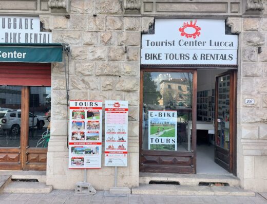 Tourist Center Lucca offering bike tours and rentals, including e-bikes, with signage for guided and self-guided tours visible outside the entrance.