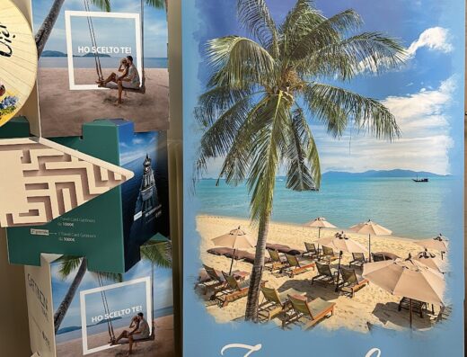 Materiale promozionale di Sanmartin Gianna, consulente viaggi: banner di Zanzibar con spiaggia e palme, cappellino Glamour, mappamondo su tavolino.