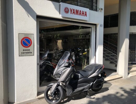 Una moto Yamaha grigia parcheggiata di fronte a un concessionario Yamaha con cartello "passo carrabile". Servizi e vendita di motocicli Traxino.