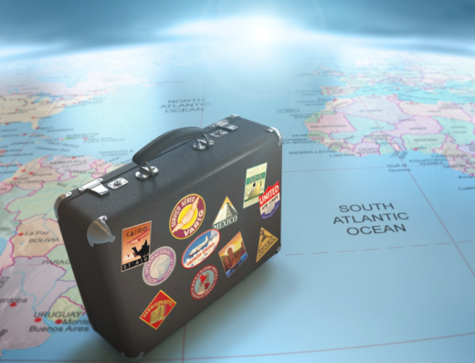 Valigia vintage nera con adesivi di viaggi su una mappa del mondo, che rappresenta i servizi di Treasure Viaggi per viaggiatori e avventurieri in moto.