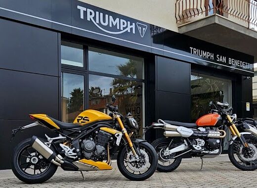 Triumph San Benedetto Motoabruzzo Srl: esposizione di motociclette Triumph, tra cui una Speed Triple RS gialla, una Scrambler arancione e una Tiger 900 Rally Pro grigia, di fronte alla concessionaria.