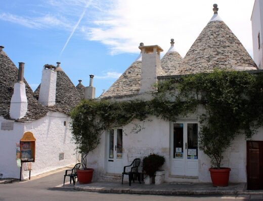 Trulli di Alberobello, Puglia, Italia: Tipiche costruzioni coniche in pietra bianca, con piante rampicanti, sedie e cielo azzurro, attrazione turistica e patrimonio UNESCO.