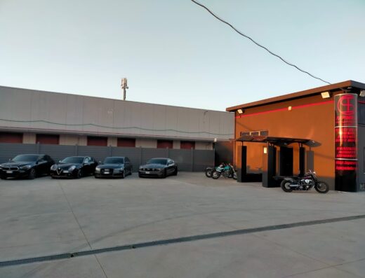 Esterno di TSPmoto & TSPcyclefarm con auto parcheggiate e due motociclette customizzate davanti all'ingresso, officina specializzata in moto e accessori moto.