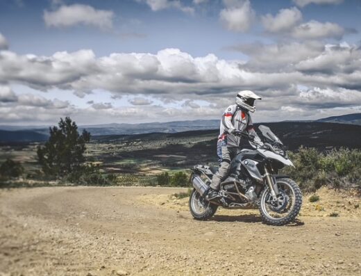 Un motociclista in sella a una moto da turismo BMW GS in Sardegna, con paesaggio collinare sullo sfondo. Noleggio moto Twist & Ride Sardinia.