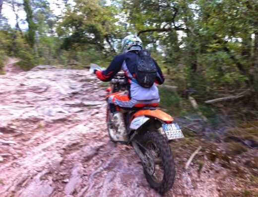 Un motociclista su una moto da enduro arancione guida su un sentiero roccioso in Umbria, durante un tour o un noleggio di moto.