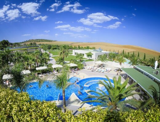 Vista aerea della piscina e dei giardini dell'UNAHOTELS MH Matera, con persone che nuotano e si rilassano al sole.