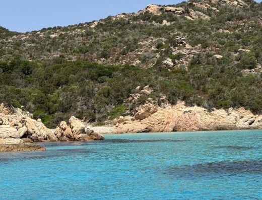 Spiaggia con acqua cristallina e rocce a Sardinia, ideale per un viaggio in moto alla scoperta delle coste sarde.