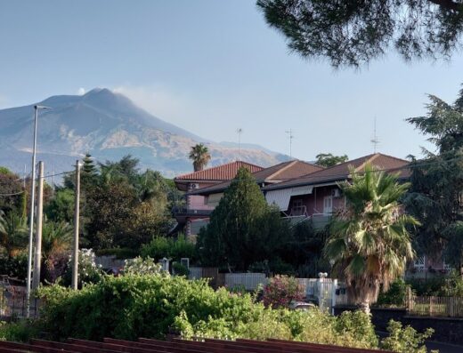 Veduta di Catania verso l'Etna, con case e vegetazione in primo piano. Offre uno scorcio pittoresco della zona, perfetto per il turismo e la scoperta del territorio.